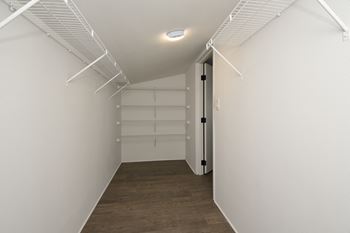 a walk in closet with white walls and a dark wood floor